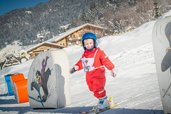 Ein strahlendes Kind in rotem Skianzug macht erste Schwünge in der liebevoll gestalteten Kinderskischule im Landgut Furtherwirt