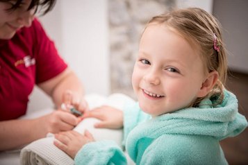 Glückliches Mädchen im flauschigen Bademantel genießt eine liebevolle Maniküre im Wellnessbereich des Landguts Furtherwirt