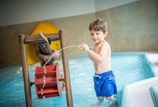 Junge spielt begeistert mit einer Wasserspritze im Kinderpool des Landguts Furtherwirt