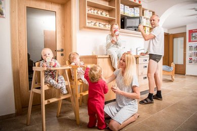 Fröhliche Familie im Landgut Furtherwirt genießt gemeinsam das Frühstück in einer gemütlichen Küche, während die Kinder spielerisch den Morgen beginnen